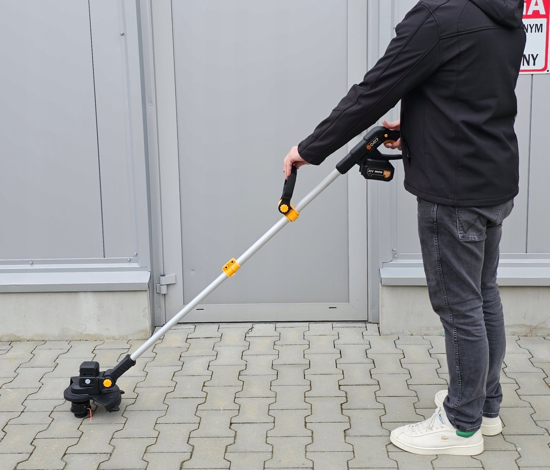 Podkaszarka przedstawiona na tle garażu. 